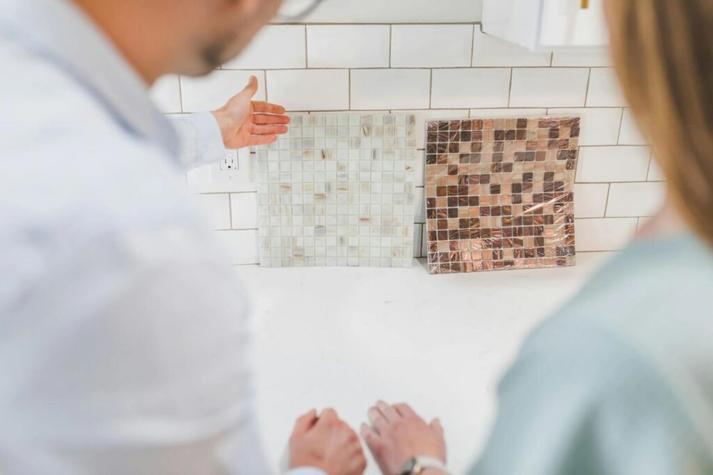 En medio de una remodelación de cocinas dos personas examinan muestras de mosaicos en una encimera blanca en su cocina alicatada deseosas de evitar errores comunes-8 Errores comunes en la remodelación de cocinas (¡y Cómo Evitarlos!)
